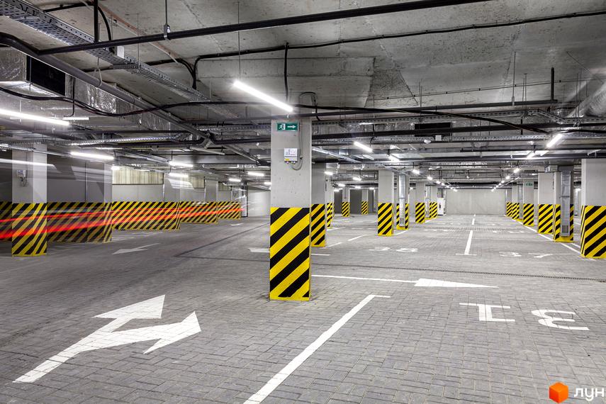 Підземний паркінг ЖК Avalon Up з позначеними місцями для паркування та колонами, оздобленими чорно-жовтими смугами. Освітлення забезпечують довгі світлодіодні лампи.