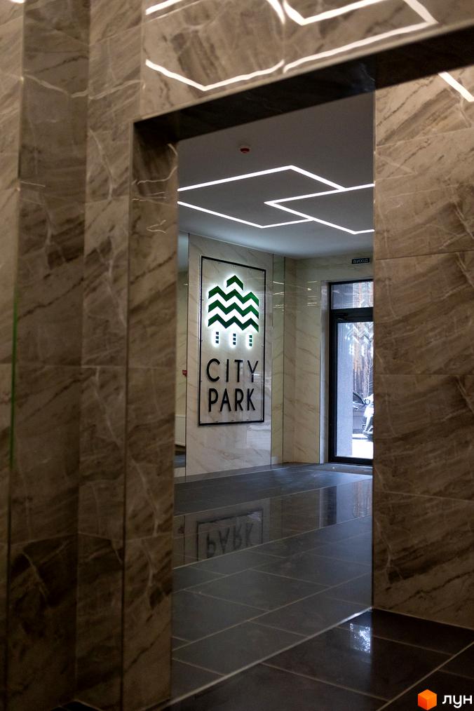 Лобі житлового комплексу City Park з мармуровим оздобленням стін та підлоги, сучасним освітленням та виходом назовні.