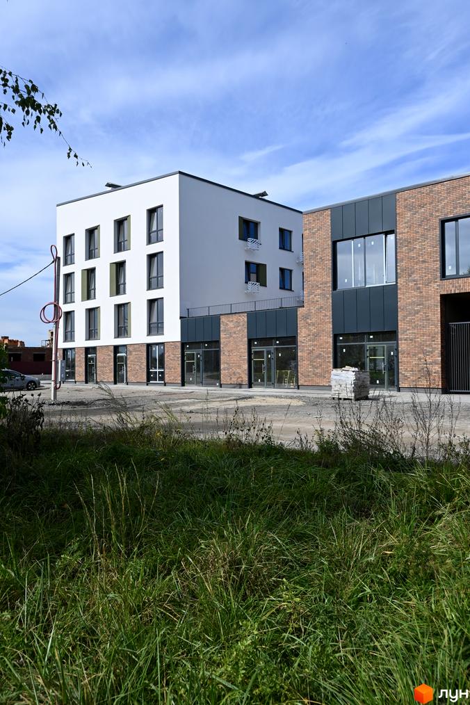 Зовнішній вигляд новобудови ЖК Субурбія з білою та цегляною фасадною частиною, великими вікнами та прибудинковою територією з травою.