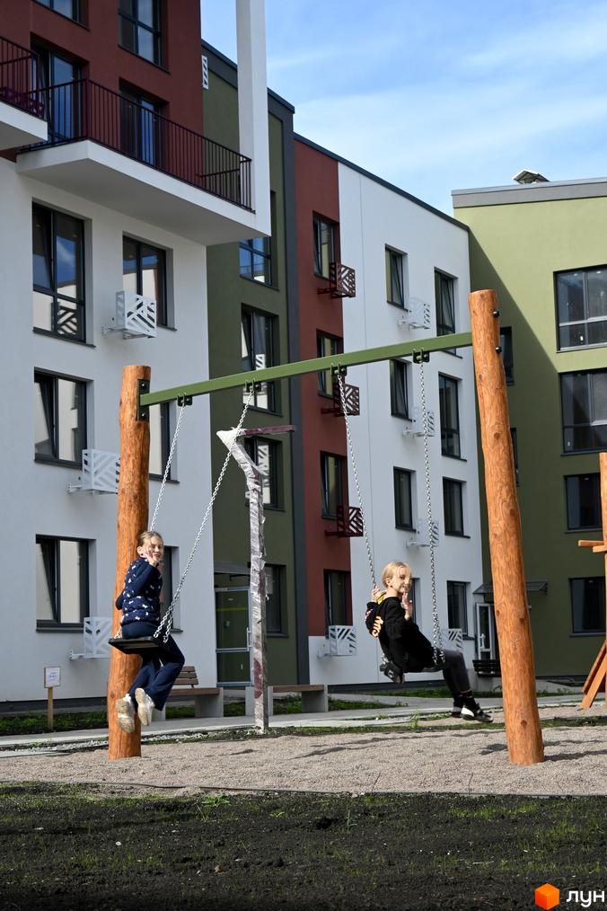 Діти граються на дитячому майданчику біля багатоповерхових будинків ЖК Субурбія. Зовнішній вигляд будинків з різнокольоровими фасадами та балконами.