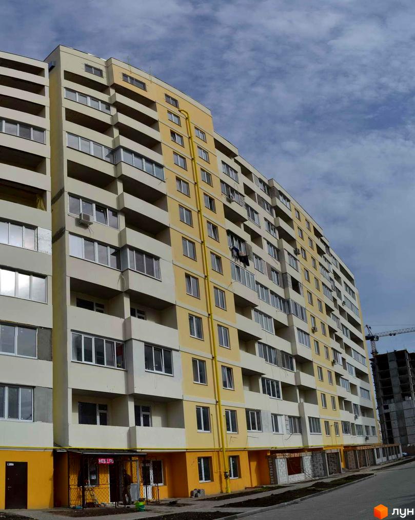 Багатоповерховий будинок ЖК Суворівський 2 з жовтим фасадом та балконами. На території видно асфальтовану дорогу та будівництво.