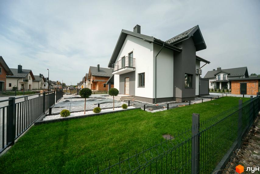 Котеджне містечко Praud Hills. Зовнішній вигляд двоповерхових будинків з сірим дахом та біло-сірими фасадами, огороджена територія з доглянутим газоном та декоративними кущами.