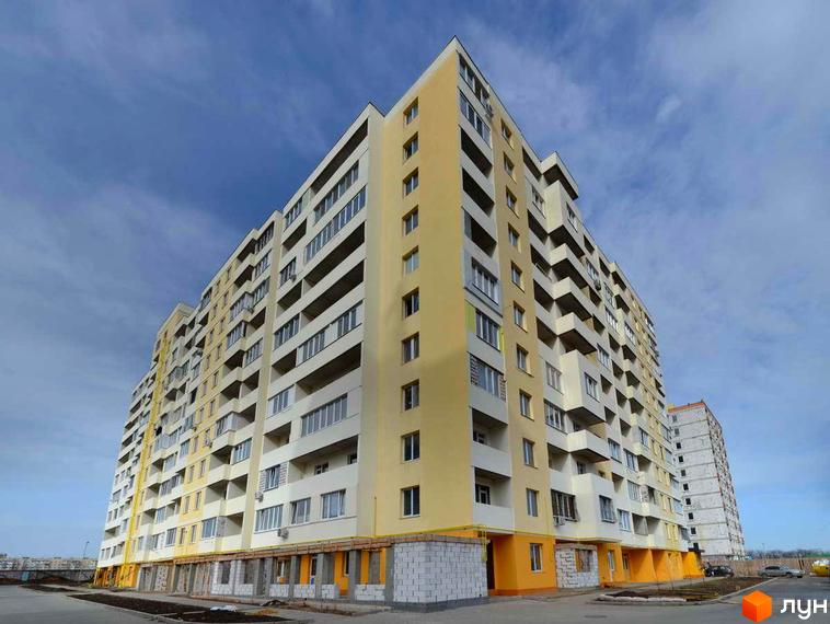 Багатоповерхова новобудова ЖК Суворівський 2 з жовтими та білими фасадами. На передньому плані видно прибудинкову територію з асфальтом.