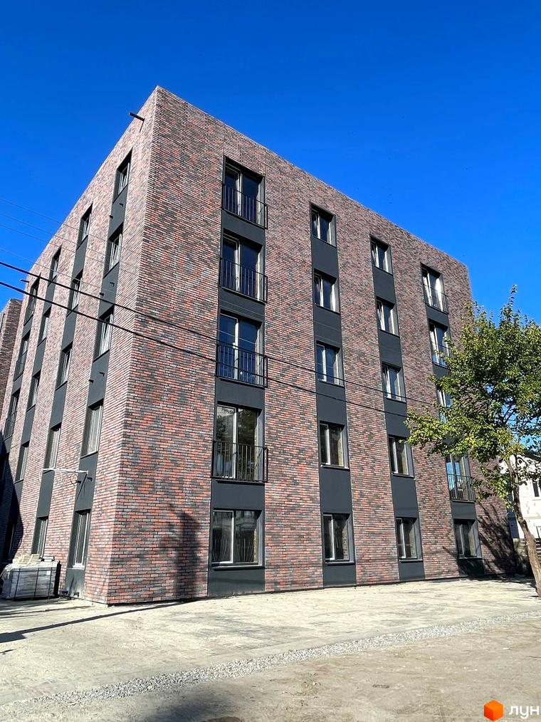 Фасад житлового комплексу Інститутська, облицьований цеглою різних відтінків, з темними віконними рамами та балконами. Навколо новобудови облаштована прибудинкова територія з тротуарною плиткою та гравійною доріжкою.