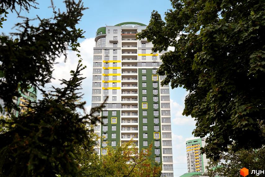 Фасад багатоповерхового Житлового комплексу Паркове місто виконаний у зелених, сірих та жовтих кольорах. Будівля розташована серед густих дерев.