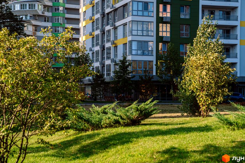 Житловий комплекс Паркове місто: багатоповерховий будинок з білими, жовтими та темно-зеленими фасадами, перед яким доглянутий зелений газон з деревами.