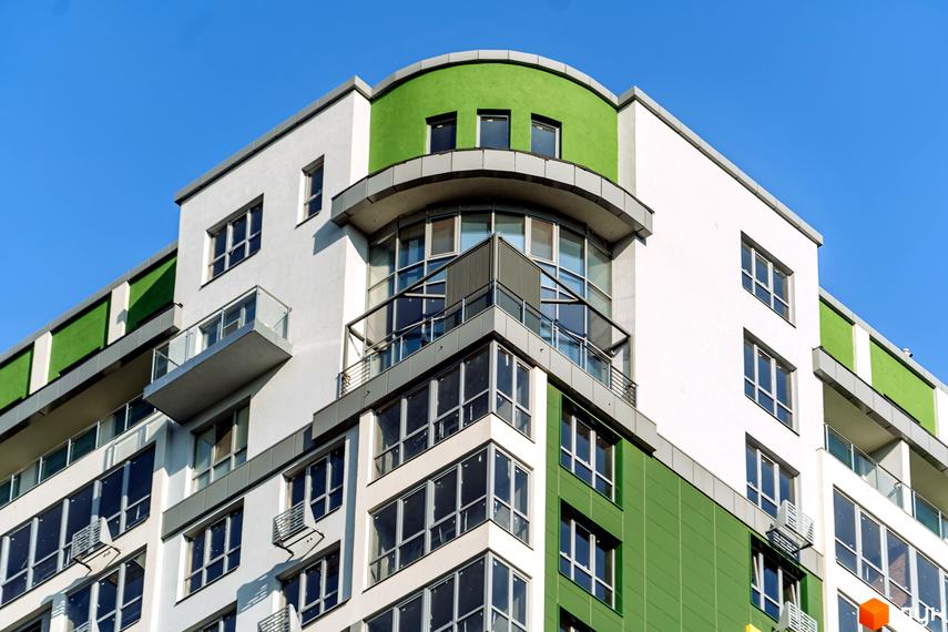 Фасад житлового комплексу Паркове місто з білими та зеленими панелями, заокругленим кутом, скляними балконами та великими вікнами.