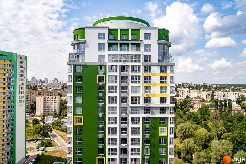 Багатоповерховий будинок Житлового комплексу Паркове місто з фасадом у білих, зелених та жовтих кольорах. Навколо будинку видно інші житлові споруди та зелені насадження.