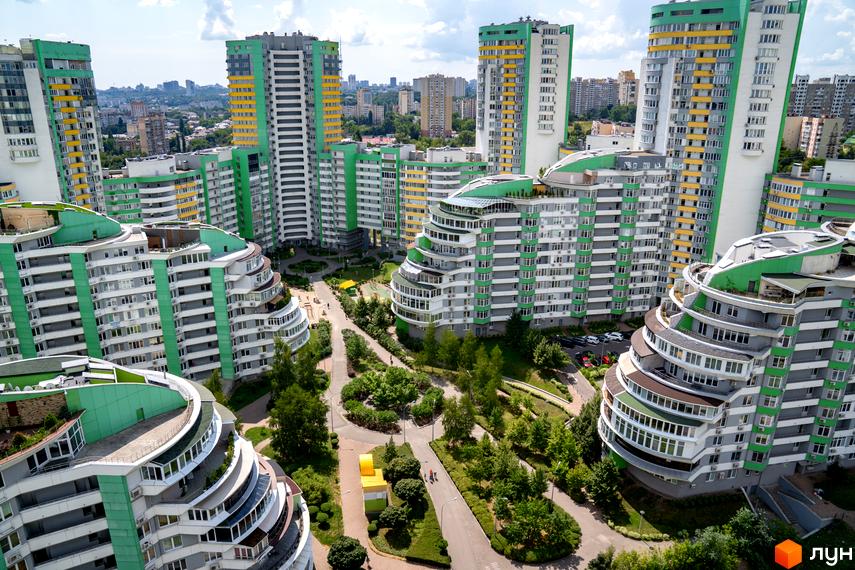Житловий комплекс Паркове місто з високими будівлями у зелено-білих та жовтих тонах. Прибудинкова територія має багато дерев та пішохідних доріжок.