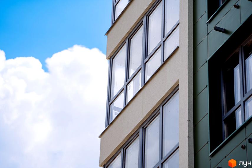 Фасад Житлового комплексу Паркове місто з великими вікнами та світлою текстурованою штукатуркою. Частина будівлі оздоблена темно-зеленими панелями під блакитним небом.