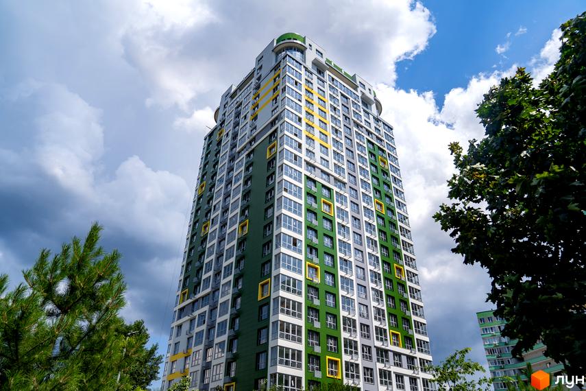 Багатоповерховий будинок Житлового комплексу Паркове місто з фасадом зеленого, сірого та жовтого кольорів. Навколо будівлі видно зелені дерева та хмарне небо.