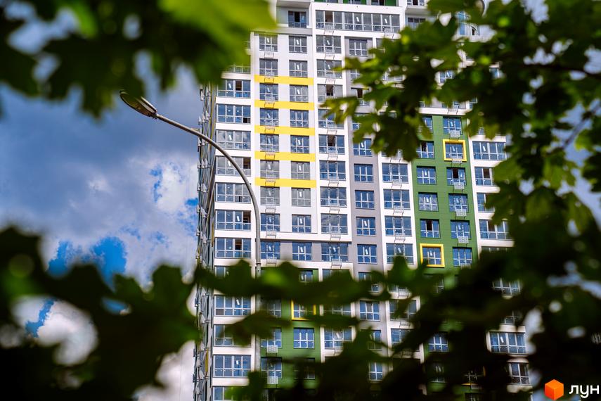 Багатоповерховий будинок Житлового комплексу Паркове місто з фасадом у білих, сірих та зелених тонах, з жовтими акцентами навколо вікон. Оточений зеленою рослинністю.