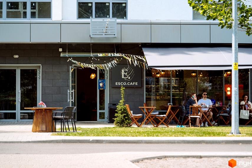 Фасад Житлового комплексу Паркове місто з кафе на першому поверсі. Прибудинкова територія має літню терасу та зелений газон.