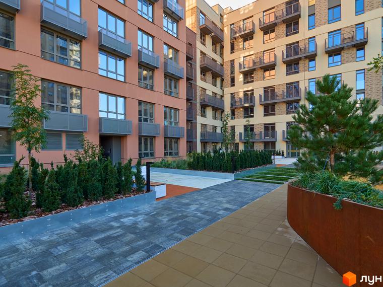 Житловий комплекс Будинок на Вавилових з фасадами світлого та теракотового відтінків, великими вікнами та балконами. Двір облаштований доріжками, деревами та кущами.