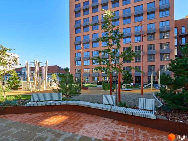 Висотна будівля ЖК Будинок на Вавилових з великими вікнами. На передньому плані облаштована прибудинкова територія з лавками та дитячим майданчиком.