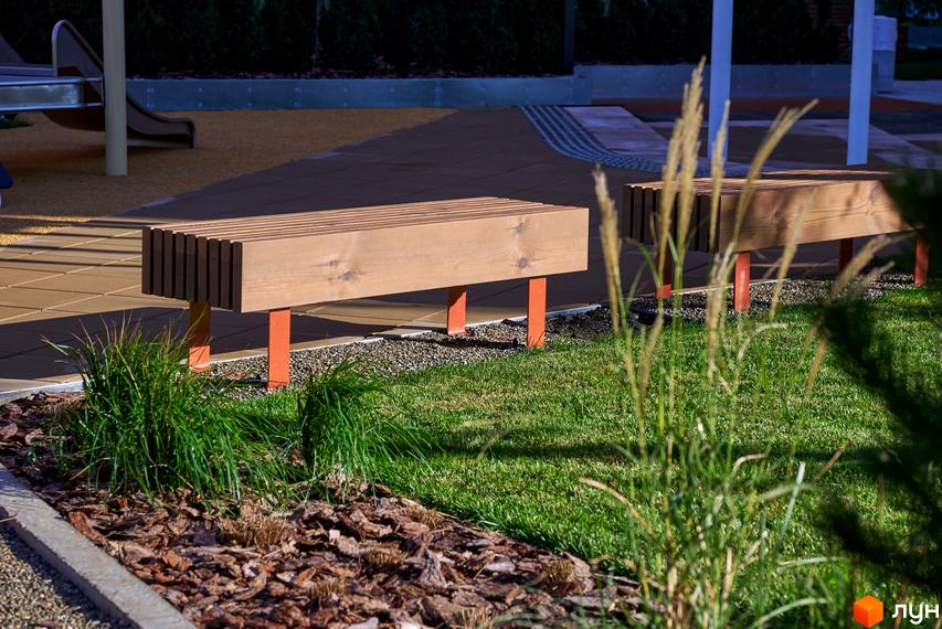 Дерев'яні лавки на території ЖК Будинок на Вавилових. Зелена галявина з рослинами та декоративним камінням.