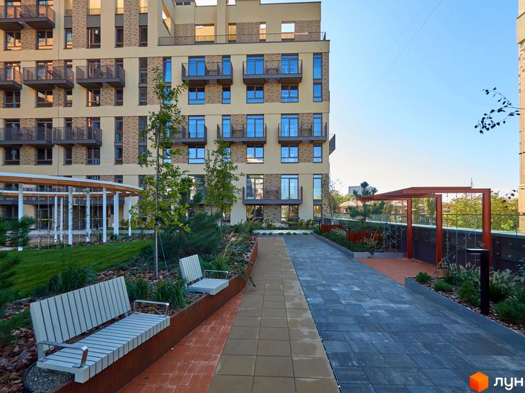 Багатоповерхова новобудова на Вавилових зі світлим фасадом та балконами. Прибудинкова територія облаштована зеленими насадженнями, лавками та доріжками.