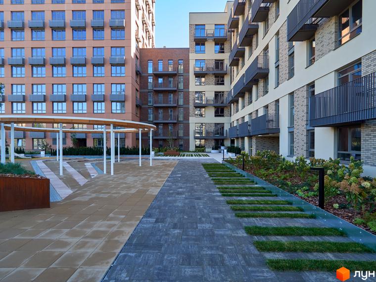 Фасади багатоповерхових будинків Будинок на Вавилових з балконами. Прибудинкова територія має доріжки, зелені насадження та альтанку.