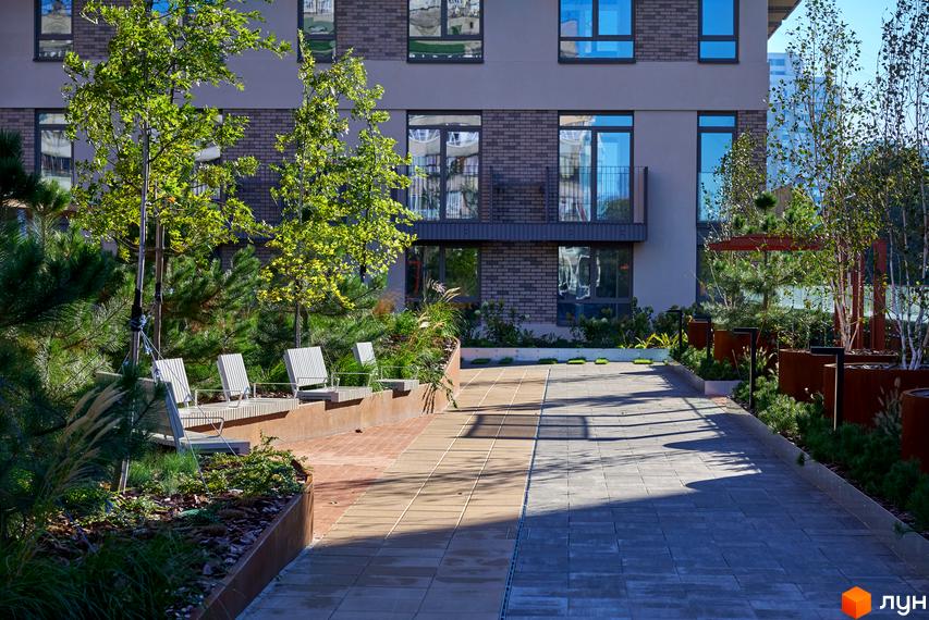 Зовнішній вигляд будівлі житлового комплексу Будинок на Вавилових з облаштованою прибудинковою територією з лавками та зеленими насадженнями.