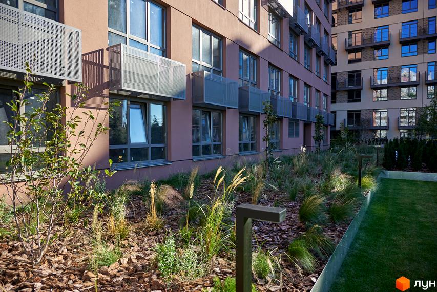 Будинок на Вавилових: світло-коричневий фасад з вікнами та сірими коробами. Прибудинкова територія з травами та газоном.