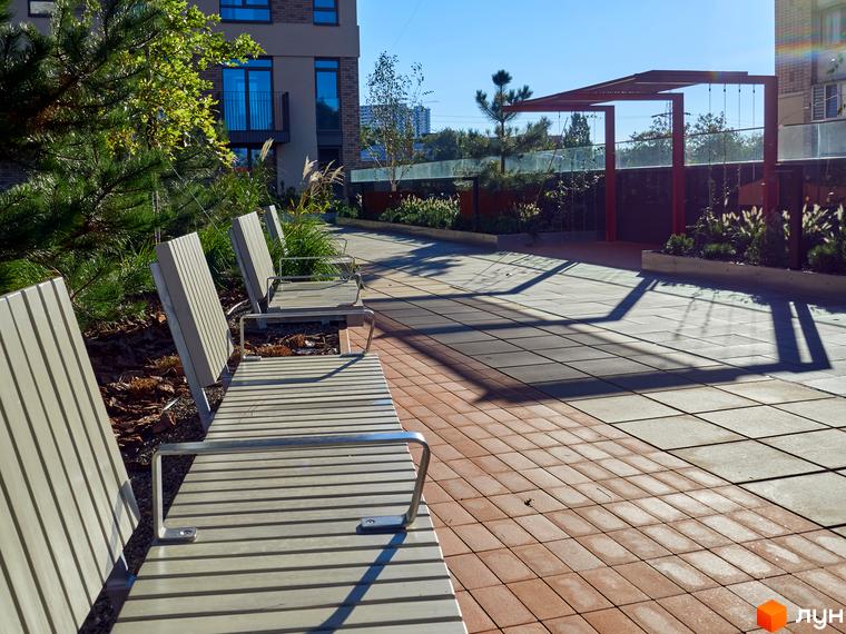 Житловий комплекс Будинок на Вавилових з фасадом у світлих тонах. На території облаштовані лави для відпочинку та доріжки для прогулянок.