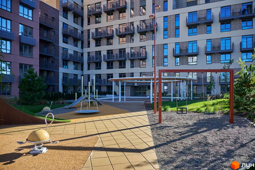 Фасади житлового комплексу Будинок на Вавилових з балконами та внутрішній двір з дитячим майданчиком, гойдалками та зеленими насадженнями.