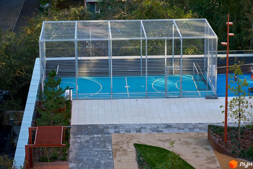 Житловий комплекс Будинок на Вавилових: вид на спортивний майданчик з огорожею та прибудинкову територію з рослинами та плиткою.