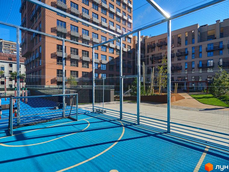 Будинки Будинку на Вавилових з червоної цегли та світлим фасадом. На прибудинковій території синій спортивний майданчик з футбольними воротами та огорожею.