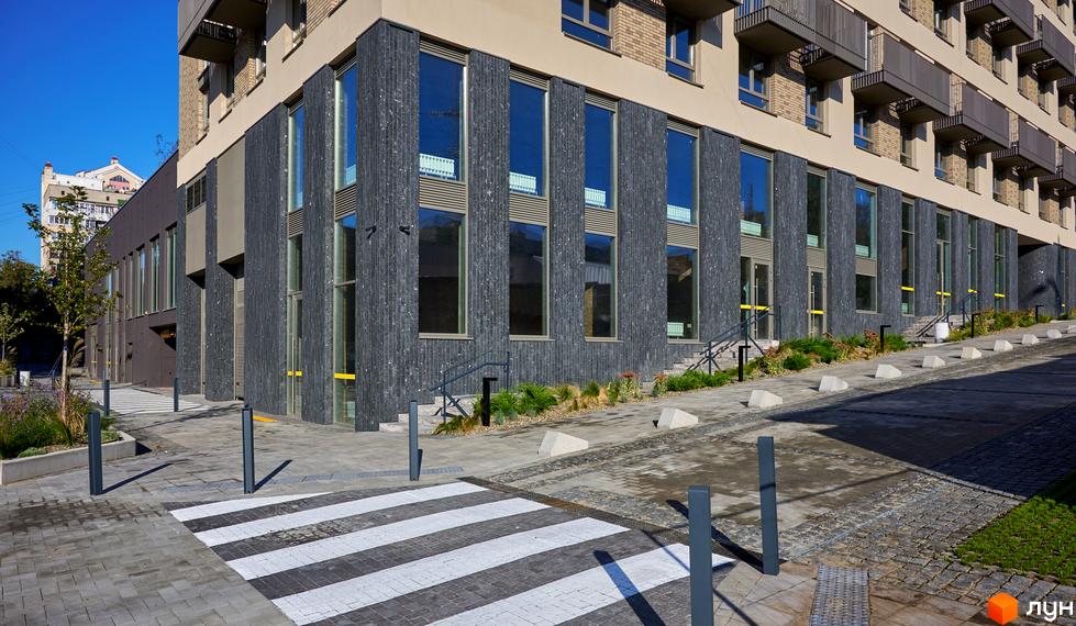 Будинок на Вавилових з темним фасадом та великими вікнами. Прибудинкова територія облаштована пішохідним переходом та озелененням.