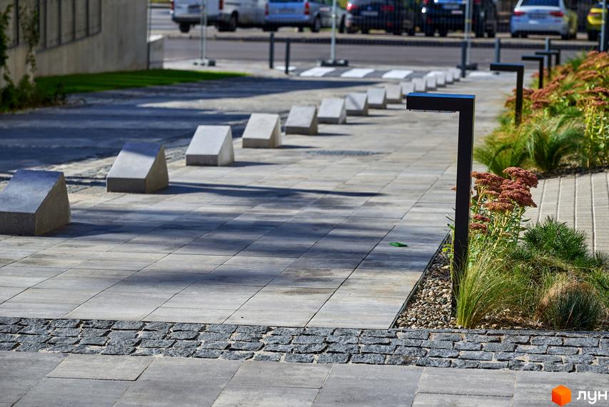 Прибудинкова територія Будинку на Вавилових: мощені доріжки, ландшафтний дизайн з рослинами та ліхтарями, бетонні обмежувачі.