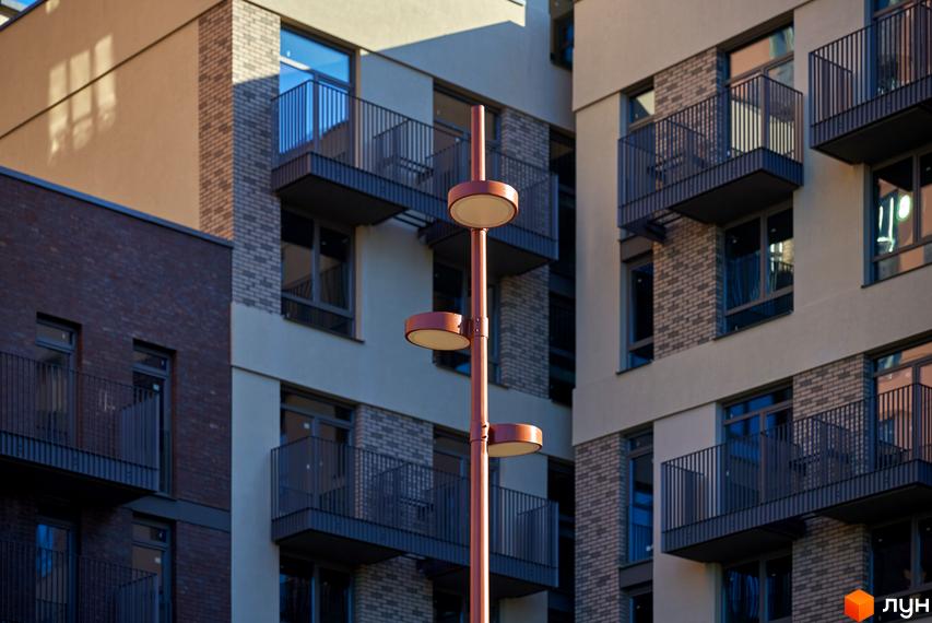 Фасад будівлі житлового комплексу з балконами та ліхтарем на передньому плані. Будинок на Вавилових - вигідне рішення для комфортного життя.