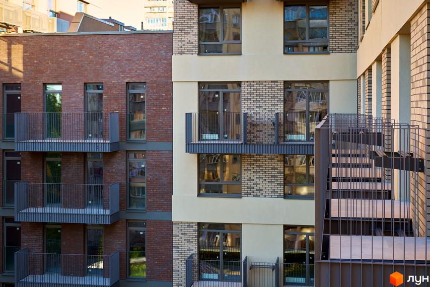 Новобудова на Вавилових: багатоповерхова будівля з фасадом з червоної цегли та світлих панелей, обладнана балконами та великими вікнами.