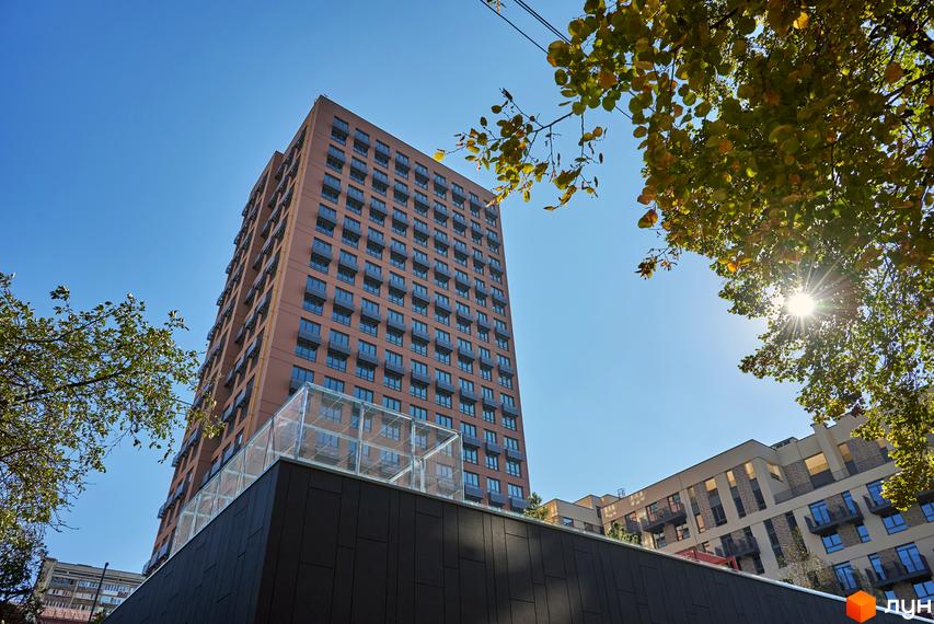 Багатоповерховий житловий будинок Будинок на Вавилових з балконами та коричневим фасадом під ясним небом. Навколо будівлі видно зелені дерева та прибудинкову територію.