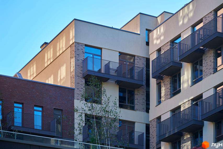 Фасад житлового комплексу Будинок на Вавилових з бежевими стінами, цегляними вставками та балконами. Перед будинком ростуть дерева.