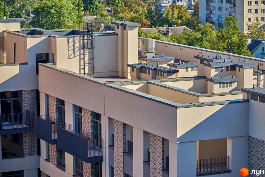 Багаторівневий фасад Будинку на Вавилових з балконами та цегляними вставками. На даху видно технічні споруди, навколо зелені дерева.