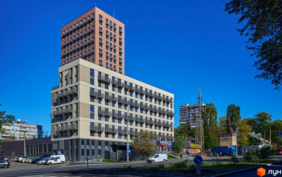 Багатоповерховий Будинок на Вавилових з фасадом світлого та коричневого кольорів, обладнаний балконами, розташований біля дороги та зелених насаджень.