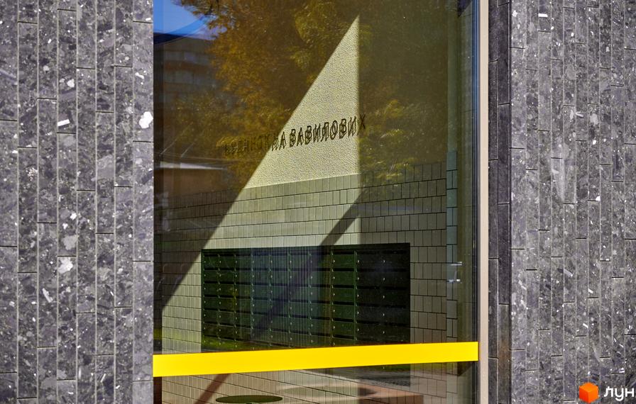 Вхід до Будинку на Вавилових зі стінами, облицьованими темними кам'яними плитами, та великим скляним фасадом. Через скло видно поштові скриньки.