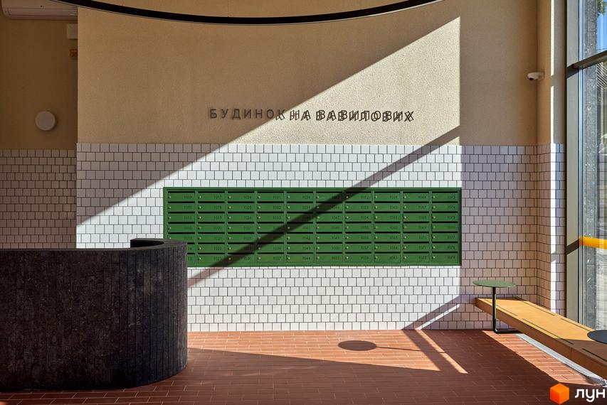 Просторий вестибюль Будинку на Вавилових з контрастною стіною з плитки та поштовими скриньками. Облаштована зона відпочинку та стійка реєстрації для мешканців.