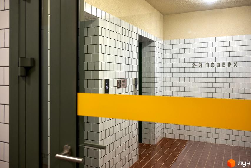 Інтер'єр ліфтового холу Будинку на Вавилових: стіни з білої плитки, коричнева підлога, двері ліфта та покажчик 