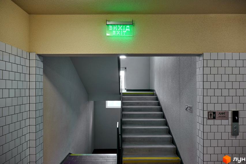 Інтер'єр загальної зони Будинку на Вавилових: сходова клітка з жовтими смугами, ліфт та стіни, облицьовані білою плиткою.