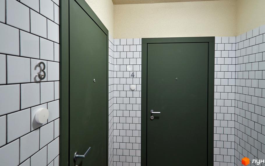 Інтер'єр коридору в Будинку на Вавилових: темні двері та стіни, оздоблені білою плиткою. Видно номери квартир 3 та 4.