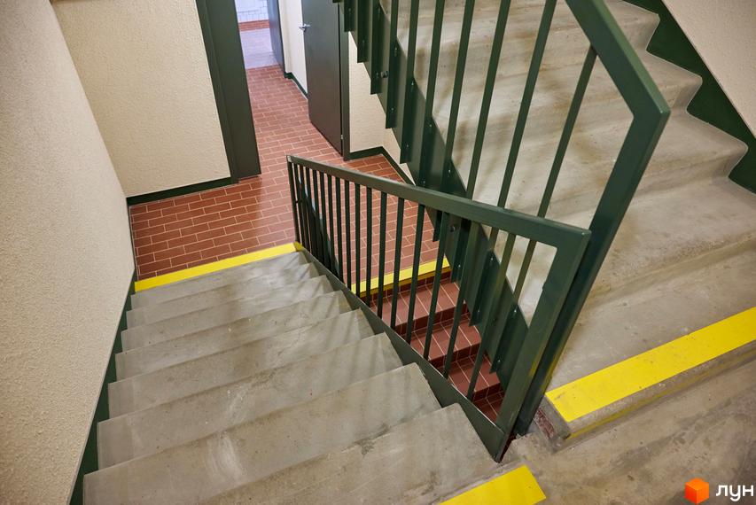 Сходи в під'їзді будинку. Сходинки бетонні, поручні металеві. На стінах світла штукатурка, підлога викладена плиткою.