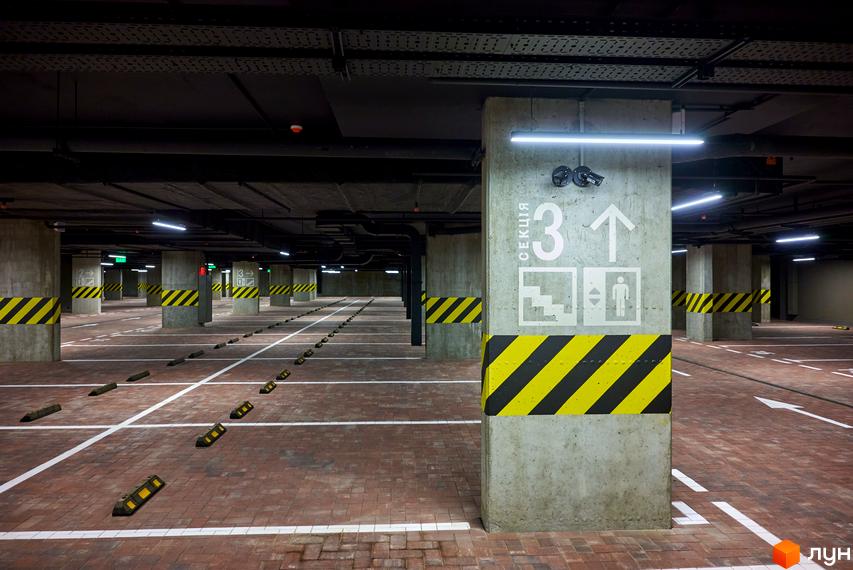 Підземний паркінг ЖК Будинок на Вавилових з розміткою та покажчиками. Просторий паркінг з бетонними колонами та яскравим освітленням.