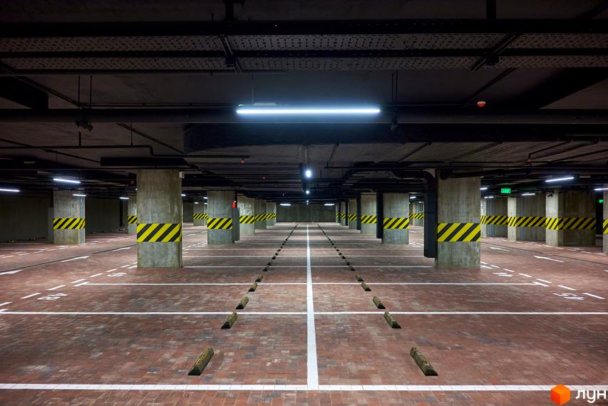 Просторий підземний паркінг житлового комплексу Будинок на Вавилових з чіткою розміткою, яскравим освітленням та бетонними колонами.