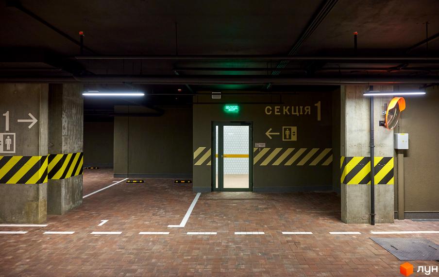 Підземний паркінг ЖК Будинок на Вавилових з розміткою для паркування та знаком секції 1. Стіни пофарбовані у темні кольори, що створює атмосферу безпеки.