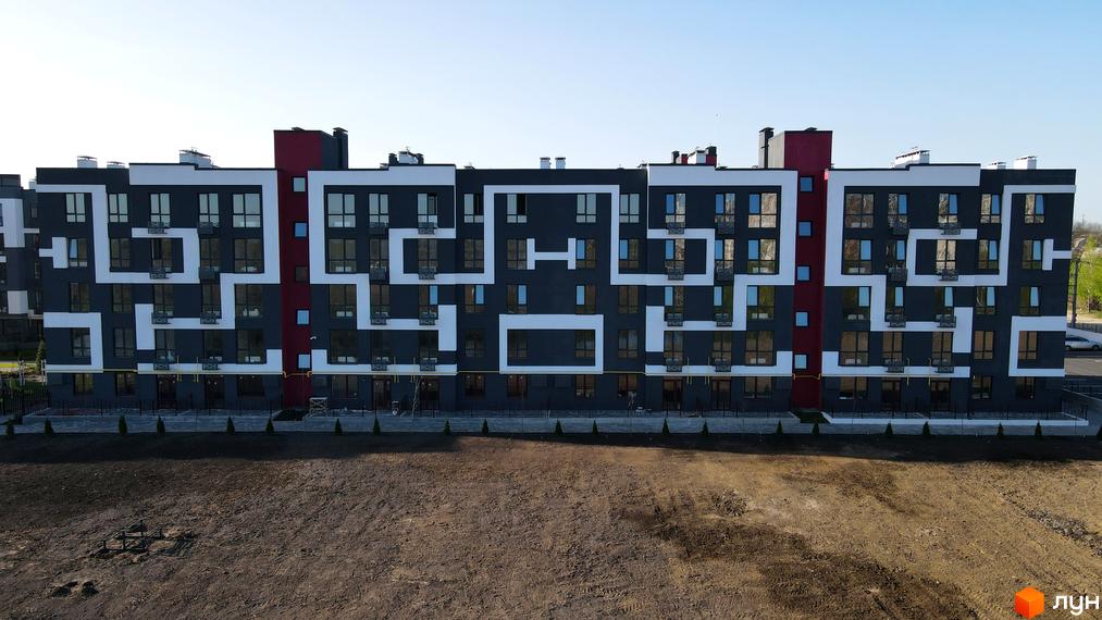 Житловий комплекс Рідний-2: фасади будинку з геометричним візерунком та прибудинкова територія з газоном.