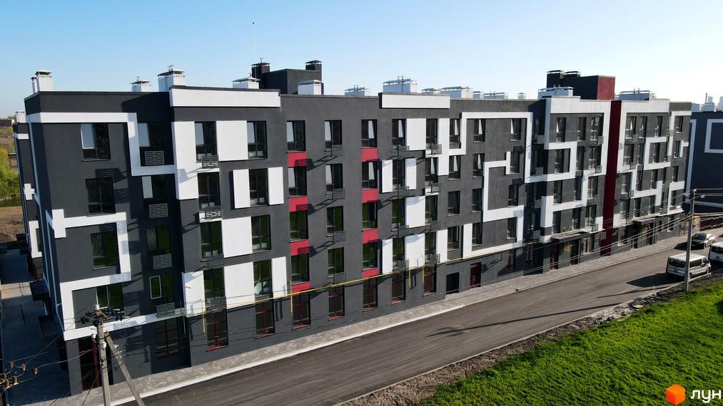 Фасад житлового комплексу Рідний-2 з вікнами та червоними вставками, поруч дорога та зелена ділянка.