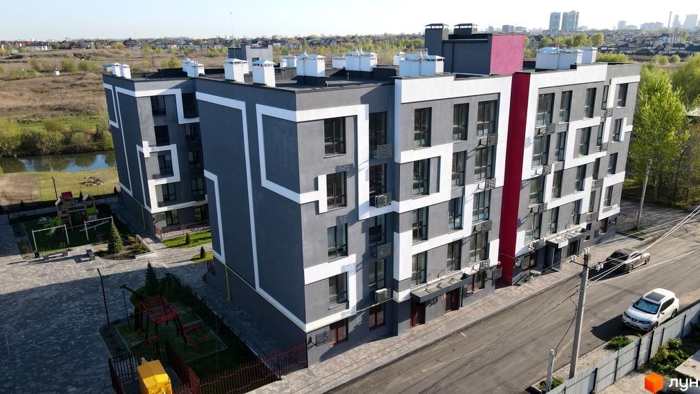 Зовнішній вигляд житлового комплексу Рідний-2 з сірими фасадами та білими декоративними елементами. На прибудинковій території розташовані дитячі майданчики та зелені насадження.