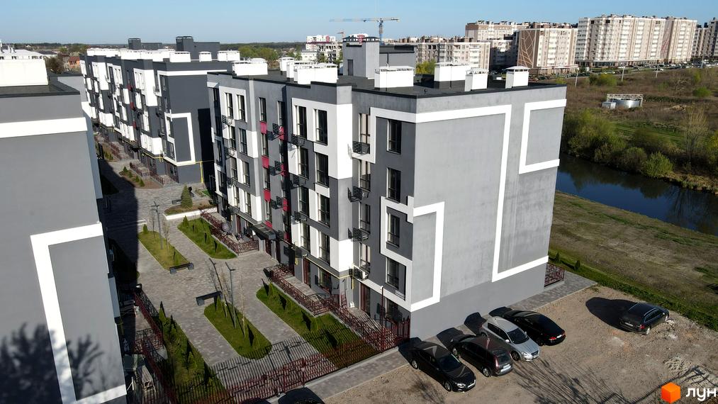 Зовнішній вигляд новобудови ЖК Рідний-2 з сірими та білими фасадами, прибудинкова територія з парковкою та зеленими насадженнями.