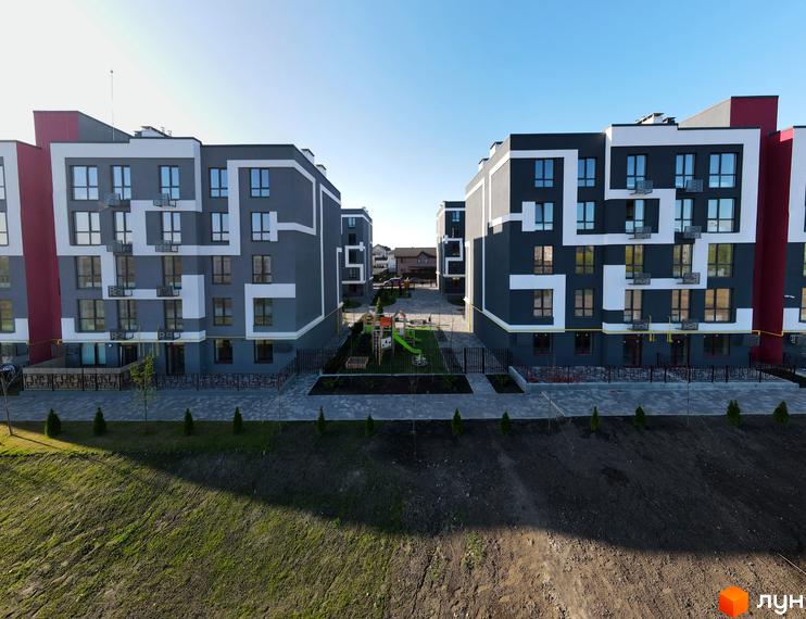Зовнішній вигляд новобудови ЖК Рідний-2 з сірими фасадами та білими декоративними елементами, прибудинкова територія з дитячим майданчиком.
